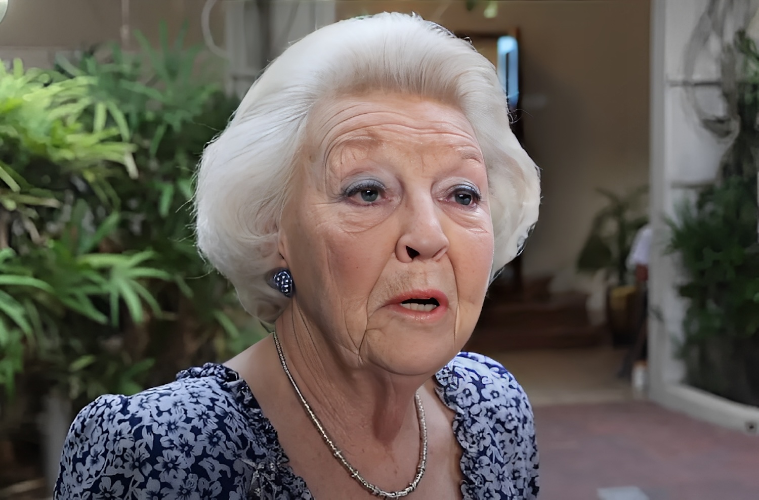 Close up of an elderly woman with white hair wearing a blue floral blouse and silver jewelry speaking outdoors