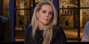 Blonde woman with long hair, wearing a dotted black top, sits in a TV studio during a discussion, looking slightly to the side.