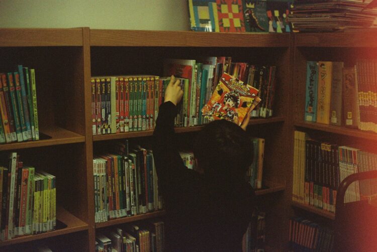 Person in black long sleeve shirt standing near brown wooden shelf