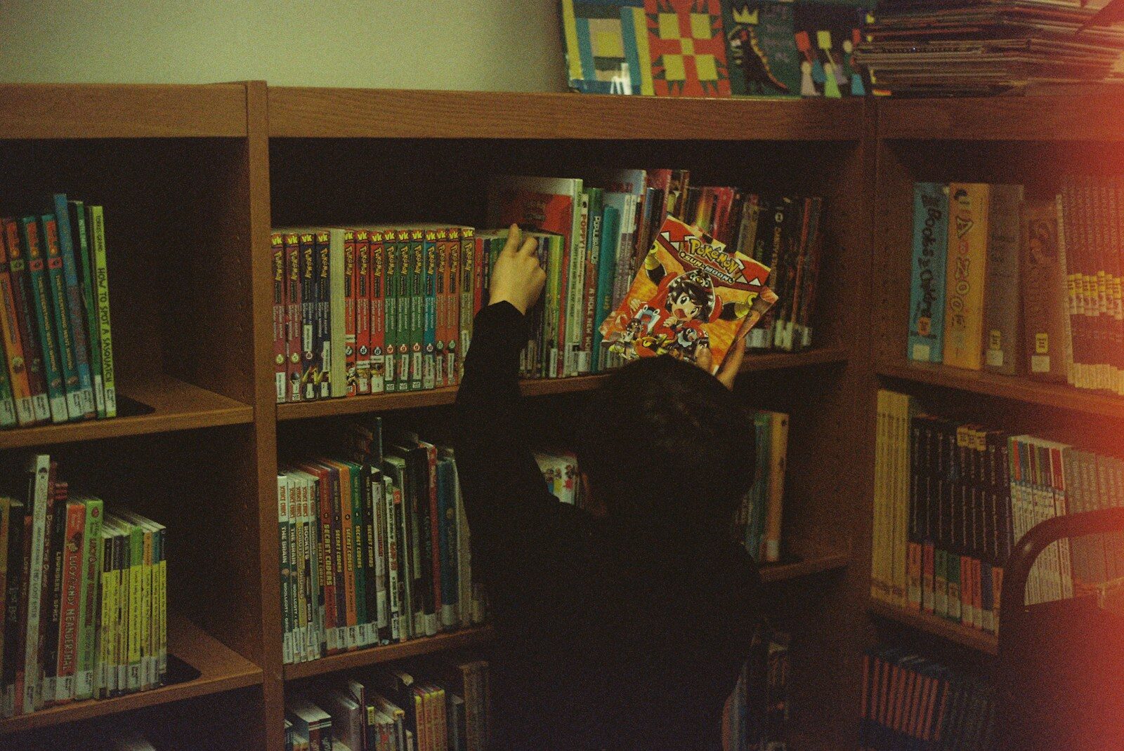 Person in black long sleeve shirt standing near brown wooden shelf