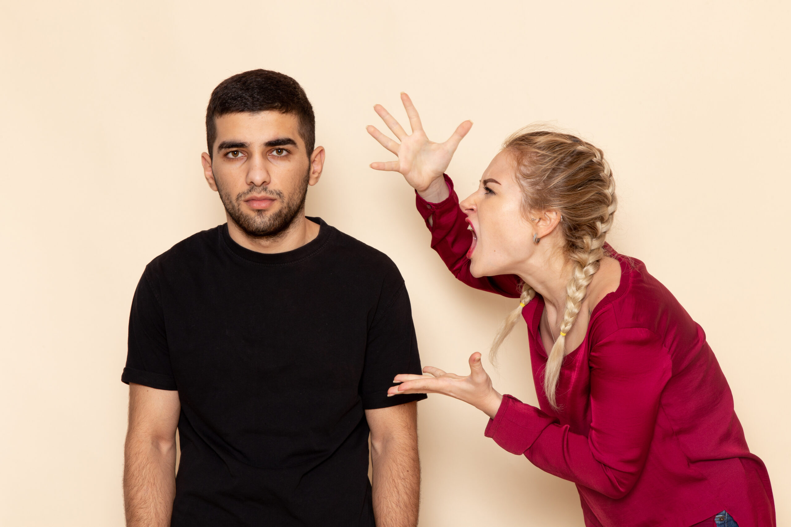 A woman with braided blonde hair wearing a red top leaning toward a man in a black shirt and shouting with her hands raised toward him