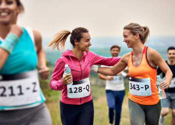 Two smiling female runners share a high five during a race each holding a water bottle
