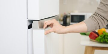 Person opening a modern white refrigerator door in a bright kitchen