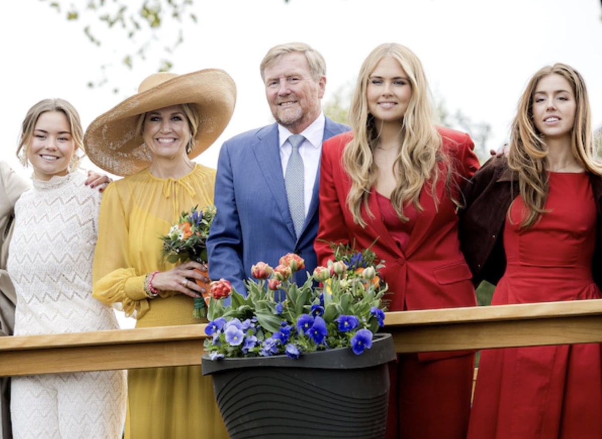 Group of people posing outdoors behind a wooden railing with a flower planter in front wearing bright coordinated outfits