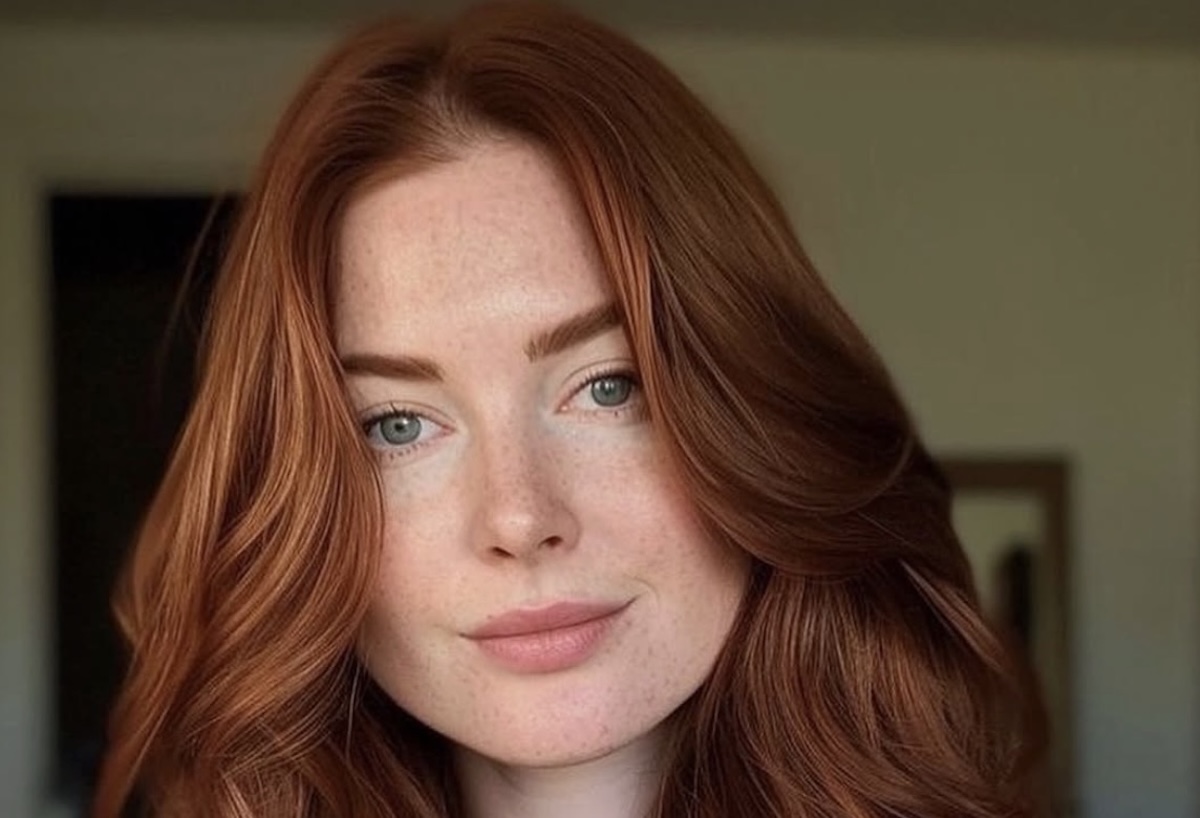 Close up portrait of a young woman with red hair and blue green eyes looking at the camera soft smile freckles visible