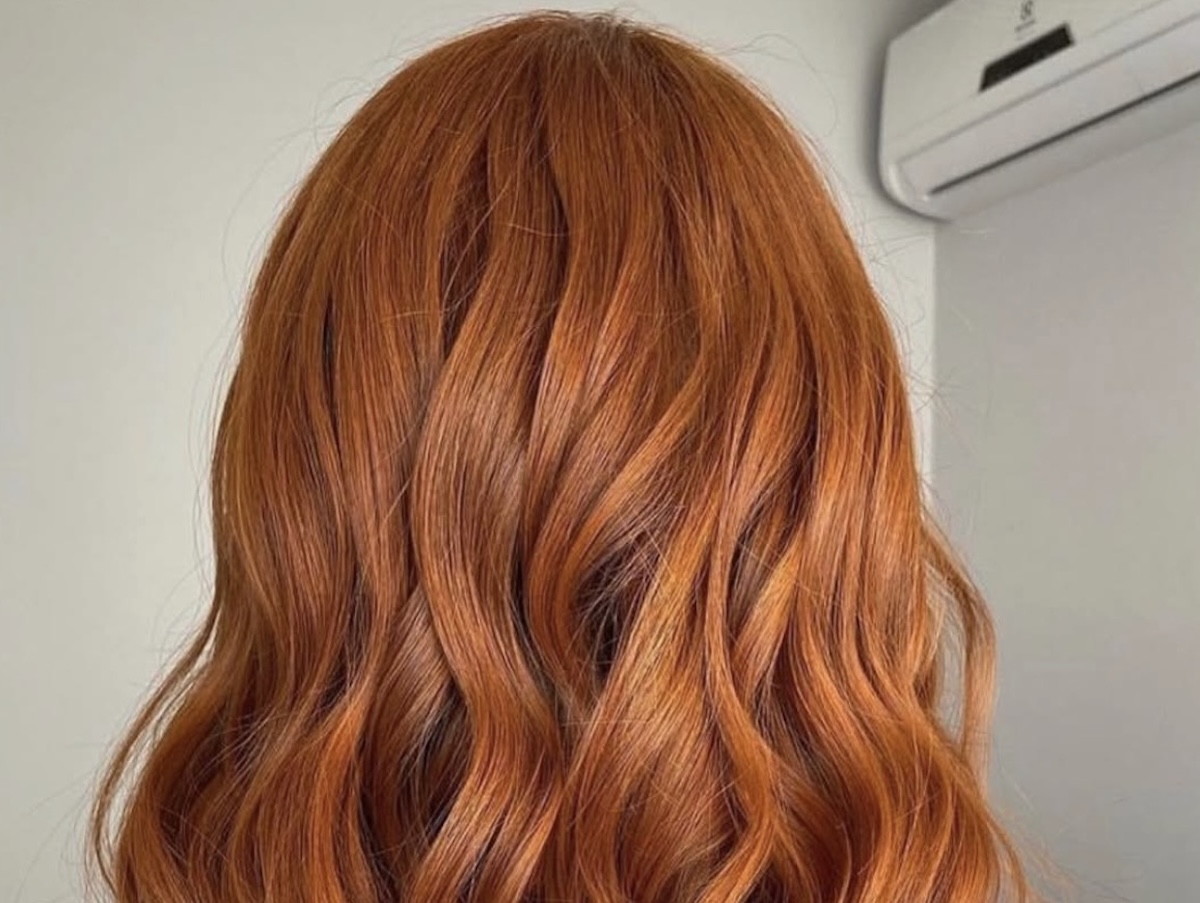 Back view of a person with bright copper red wavy hair cascading over the shoulders