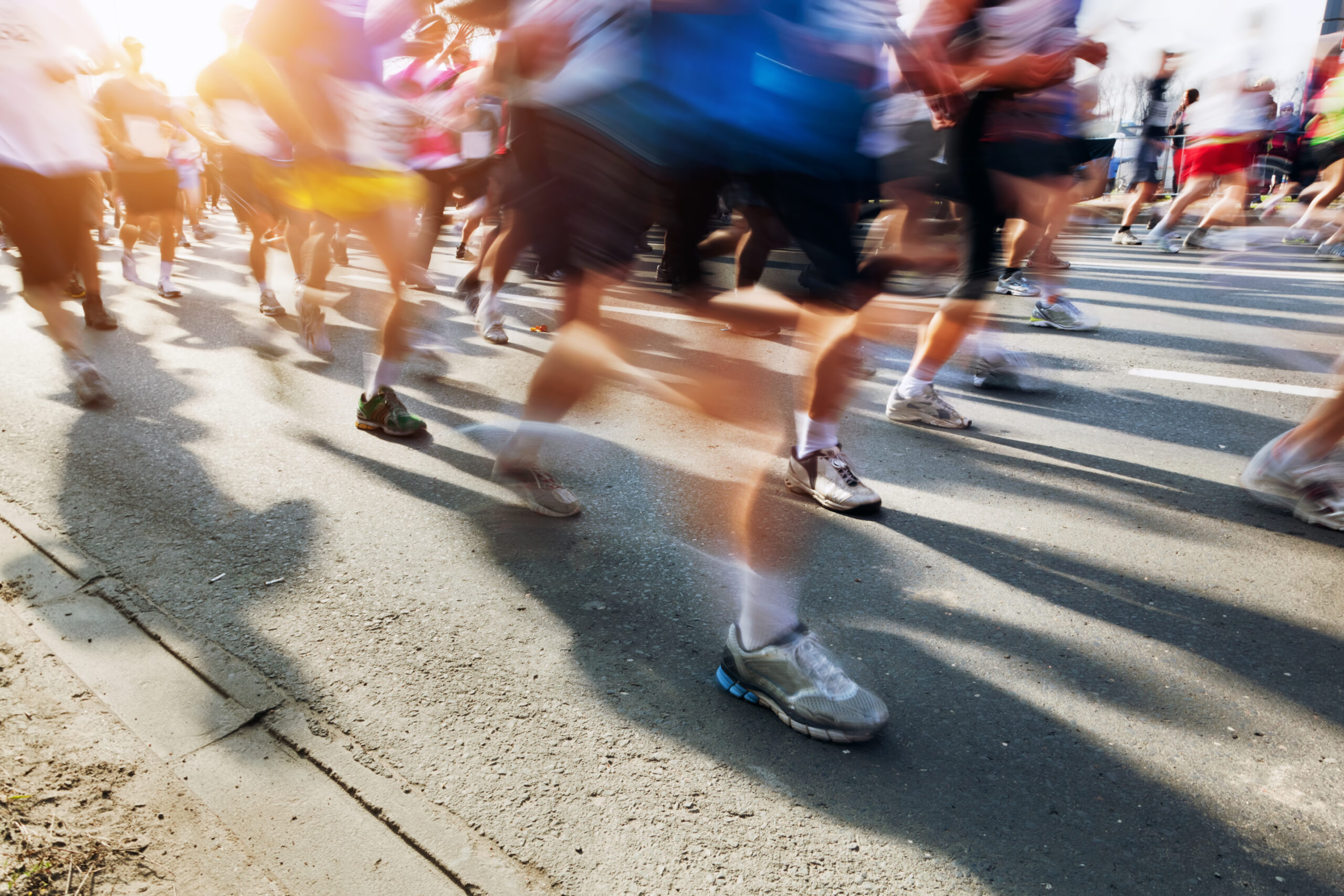 Runners in a street race captured with motion blur sun glare on the left showing legs and sneakers in motion across the road