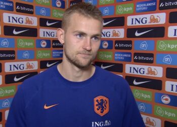 Portrait of a dutch footballer in a blue netherlands jersey standing before a sponsor wall full of ing and nike logos