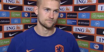 Portrait of a Dutch footballer in a blue Netherlands jersey, standing before a sponsor wall full of ING and Nike logos.