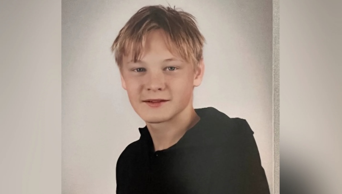 Young boy with blond hair wearing a black hoodie looking at the camera against a neutral backdrop in a studio portrait