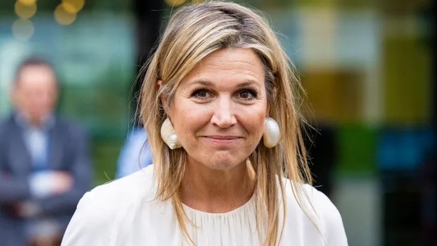 Close up portrait of a smiling blonde woman in a white blouse wearing large shell earrings outdoors