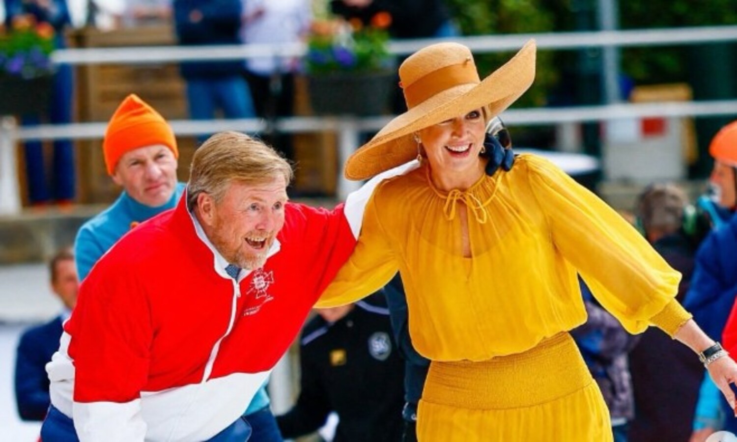 Couple skating outdoors woman in a wide brim straw hat and mustard yellow dress smiling as they glide together