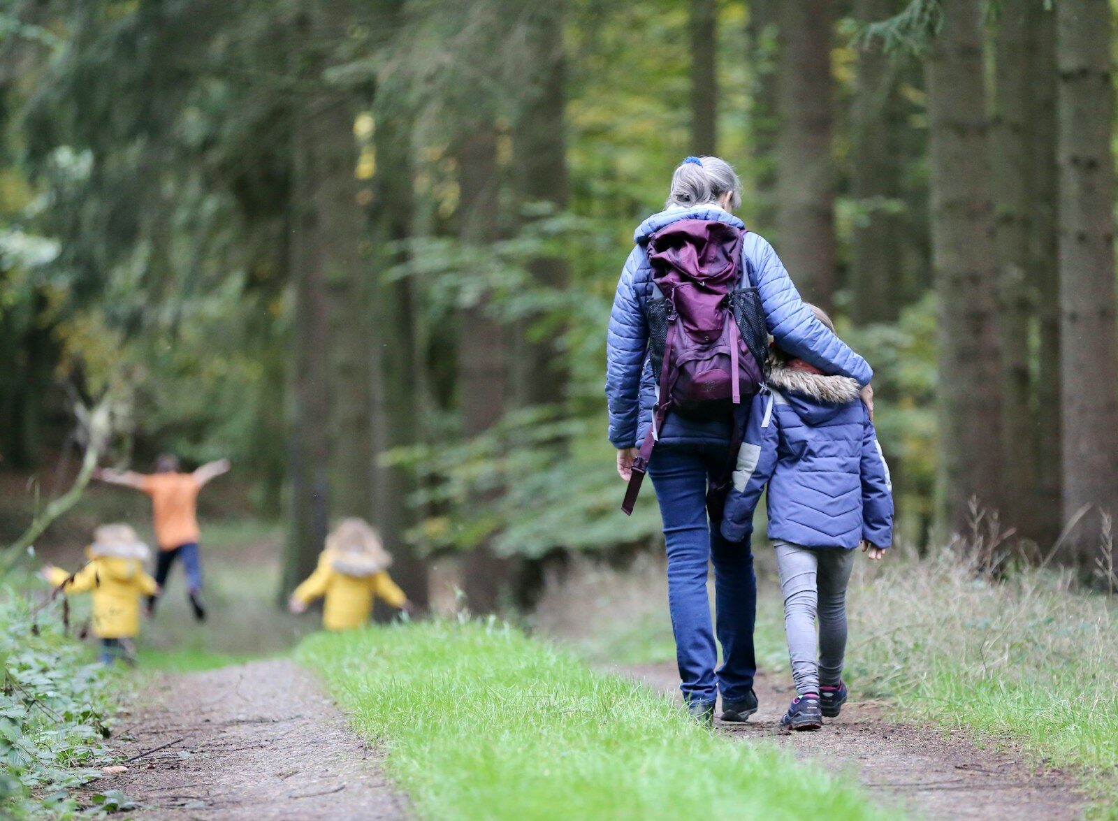 Woman in blue denim jeans and black jacket walking with woman in green jacket