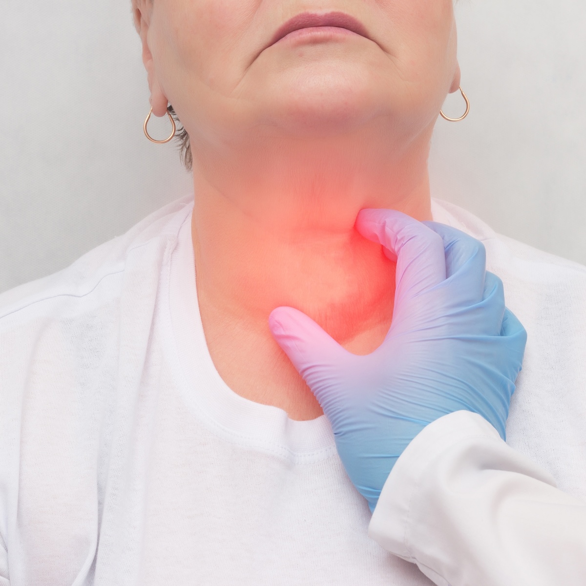 Medical professional in a blue glove pressing a patients throat with a red glow indicating neck pain area