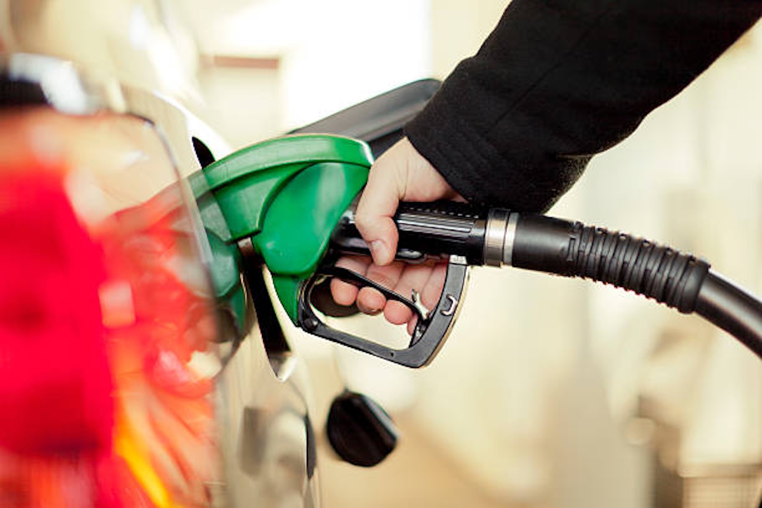 Person inserting a green fuel nozzle into a car's gas tank to refuel it.