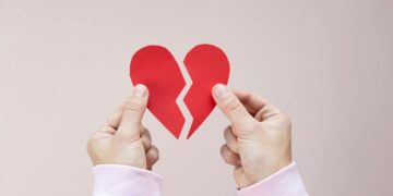 Crop unrecognizable person demonstrating red handmade parts of paper heart against white background