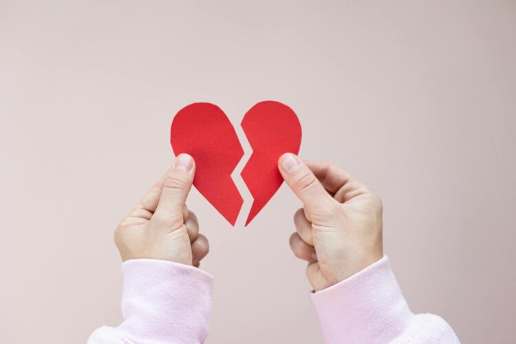 Crop unrecognizable person demonstrating red handmade parts of paper heart against white background