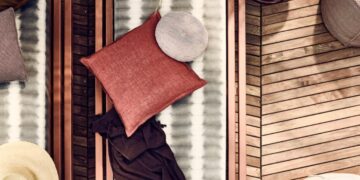 Overhead view of a wooden deck with striped cushions, pillows, and hats arranged on lounge furniture.