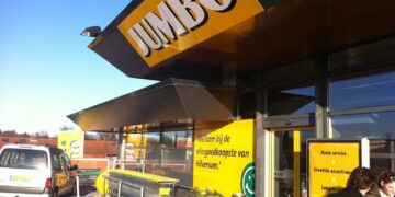 Exterior of a Jumbo supermarket with a large yellow sign, shopping carts lined up outside, and customers near the entrance.