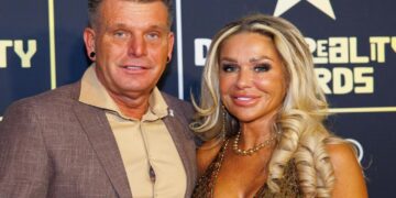 Man and woman posing on a red carpet at an awards event, both smiling.