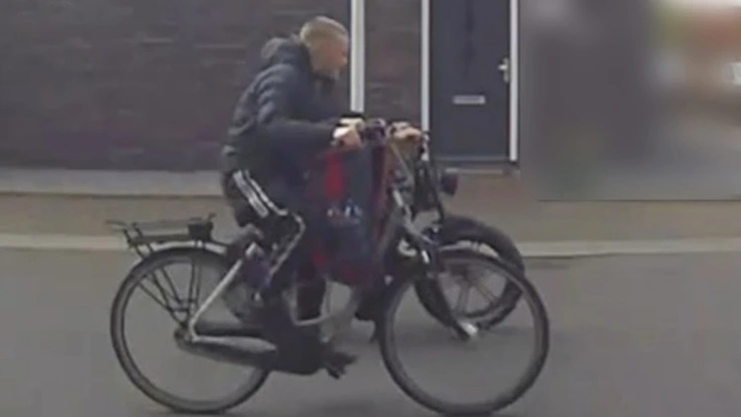 Person riding a long-tail bicycle with bags attached at the back on a city street.