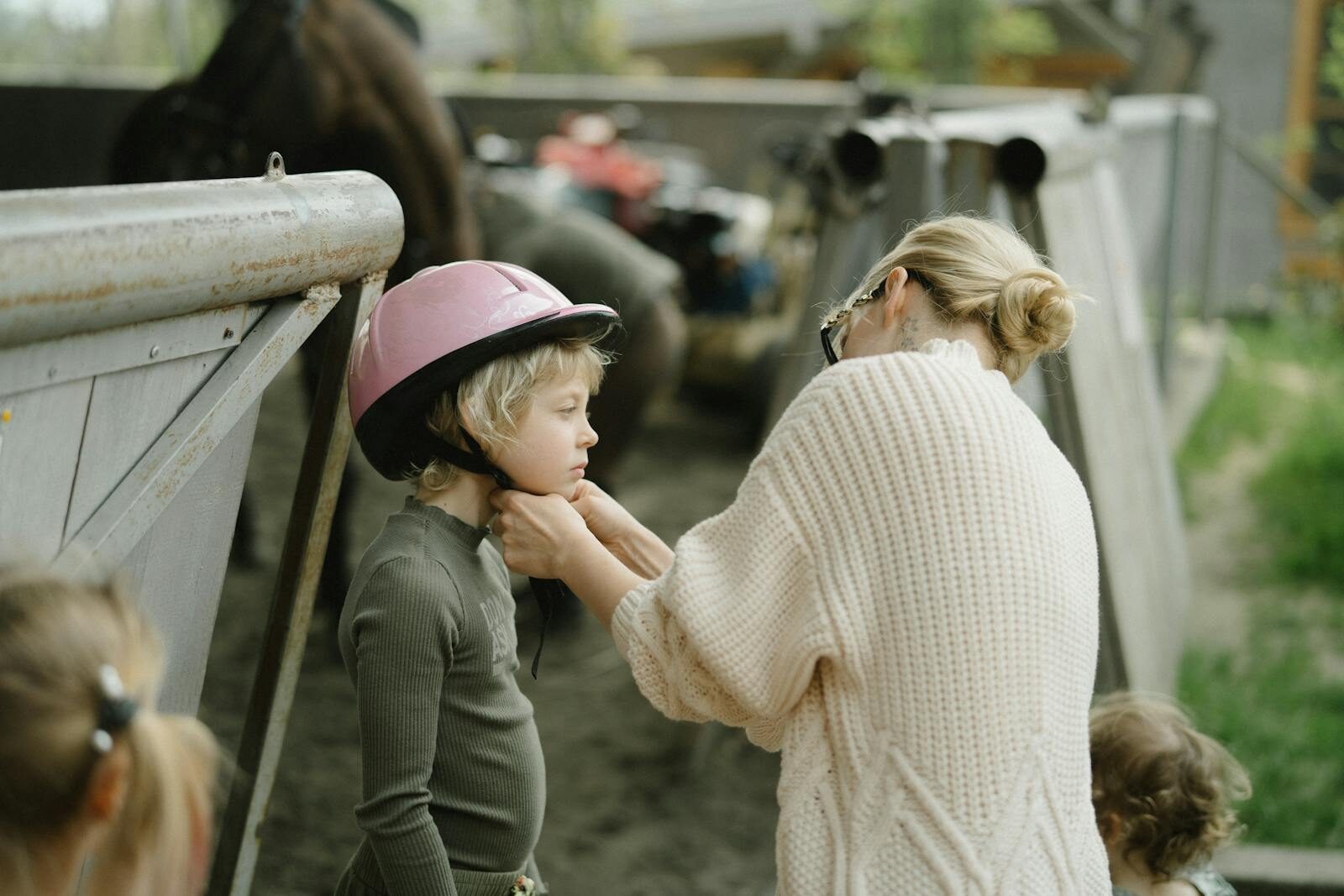 Mother helping child with a pink helmet in a farm setting, emphasizing care and safety.