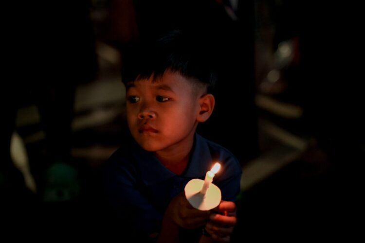 A young boy holds a lit candle in the dark.