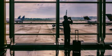 silhouette of person standing in front of glass while taking photo of plane