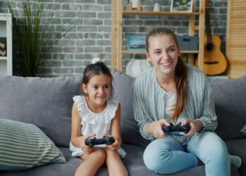 Mother and daughter playing video games together on sofa.