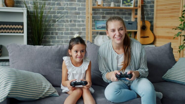 Mother and daughter playing video games together on sofa.