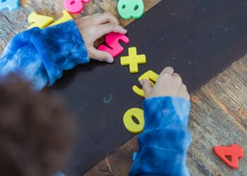 High angle of crop anonymous ethnic kid making mathematical multiplication with colorful plastic numbers during learning process
