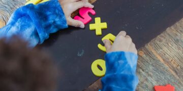 High angle of crop anonymous ethnic kid making mathematical multiplication with colorful plastic numbers during learning process