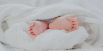 barefooted baby covering white blanket