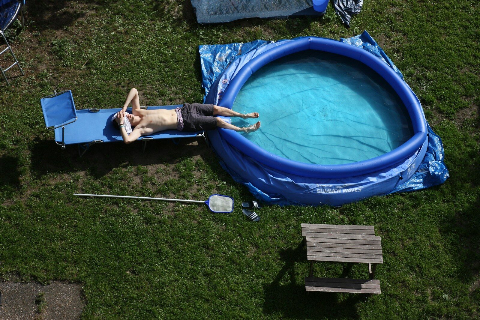 Person relaxing on a lounge chair by an inflatable pool.