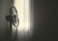 white wall fan turned on near white window blinds